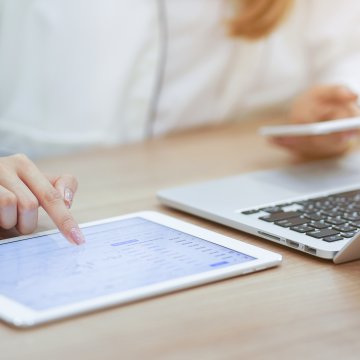 Sage Business Cloud Accounting Software features woman at desk in office on laptop and tablet with smartphone in hand